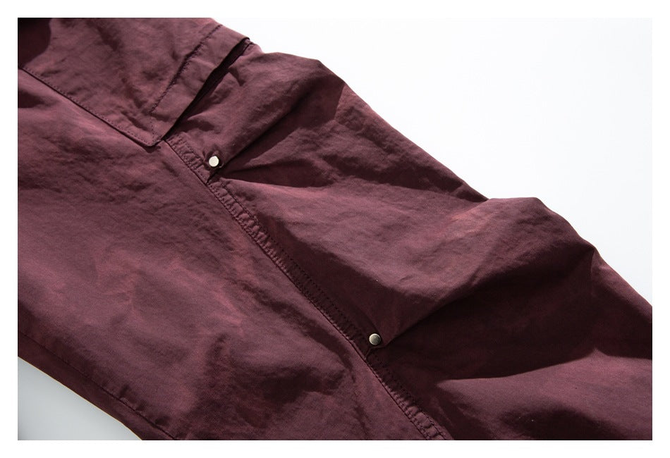 Close-up of burgundy pants fabric with a stitched seam and two small metal snap fasteners.