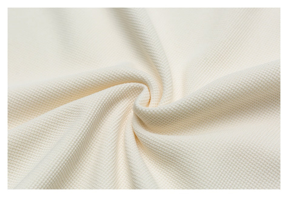 Close-up of ivory fabric with a fine waffle-like texture, draped into soft folds.