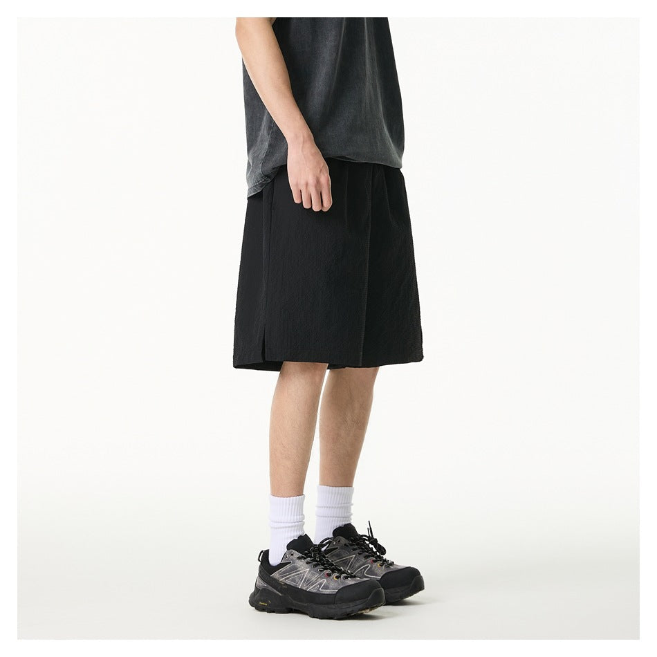 Side view of model wearing black knee-length shorts with a hem slit, gray tee, white socks and sneakers
