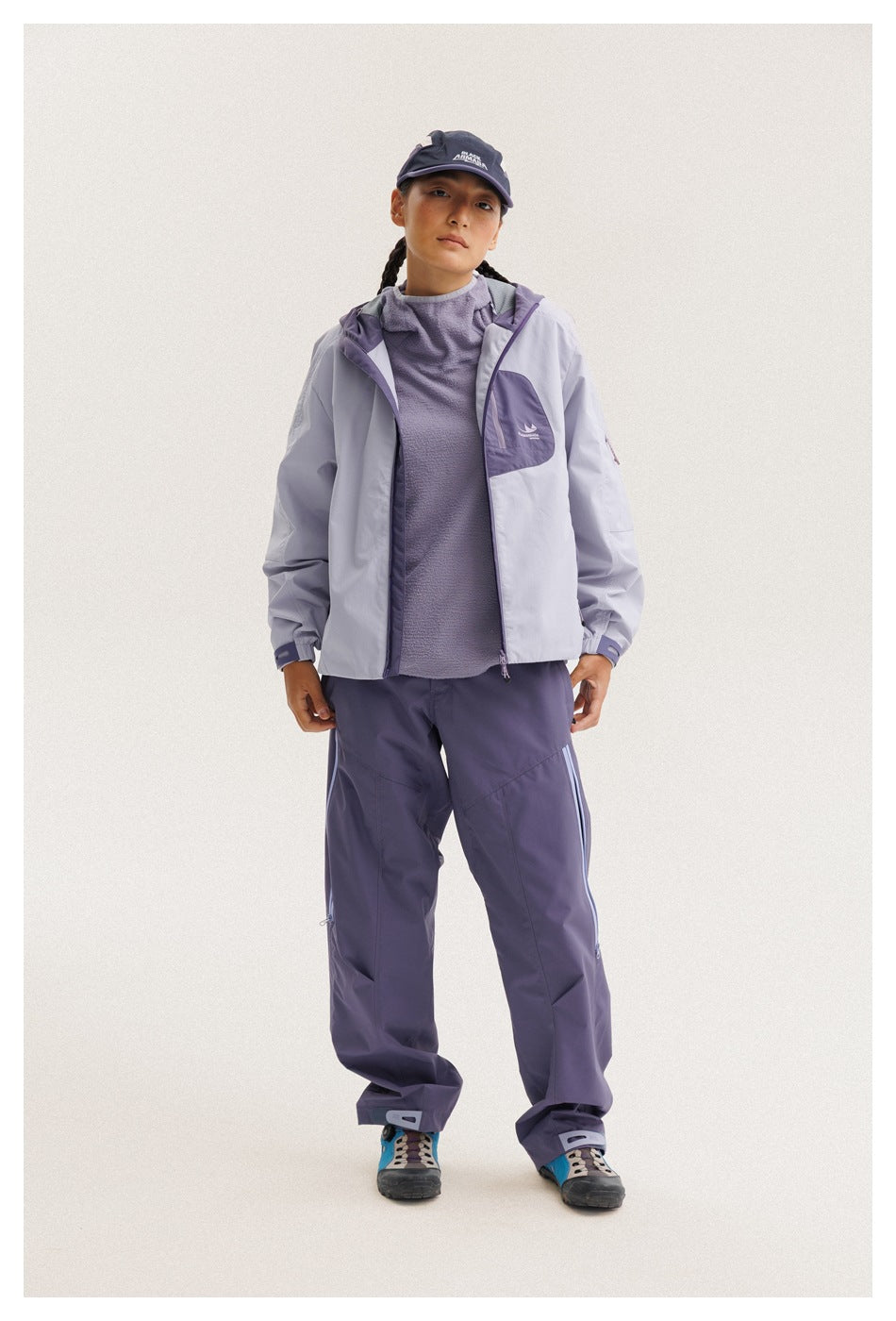 Model wears an open light lavender jacket over a purple top with matching purple pants.