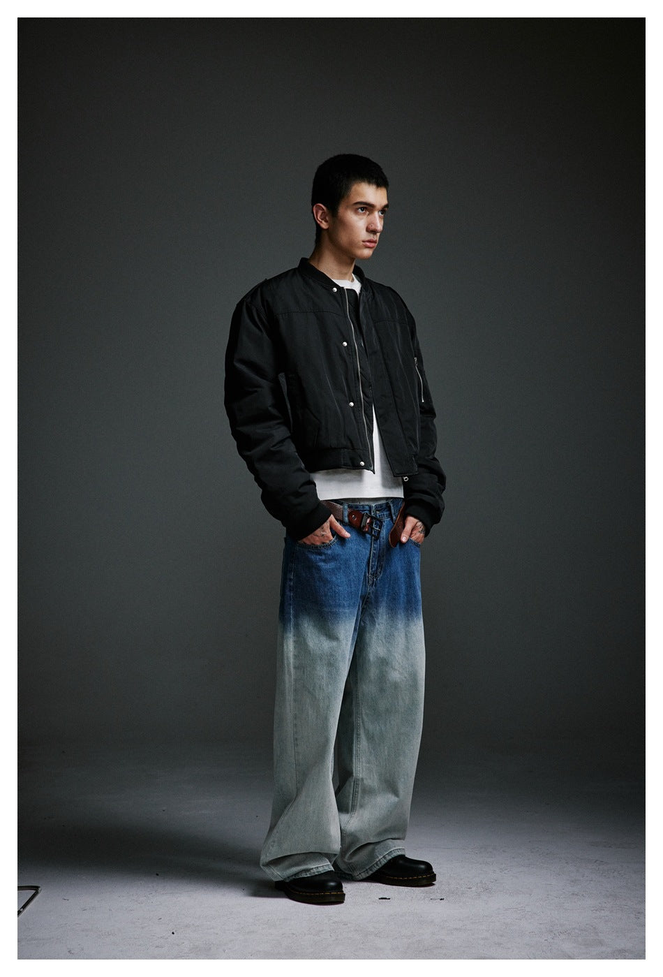 Model wearing a black snap-front jacket, white shirt, and very wide blue-to-pale-wash jeans.