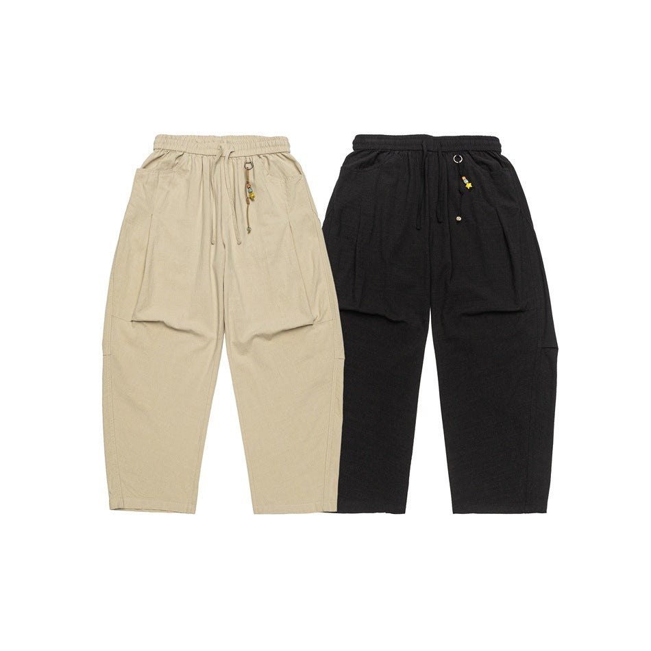 Front view of relaxed cropped pants in beige and black, with elastic waists, drawstrings and large pockets.