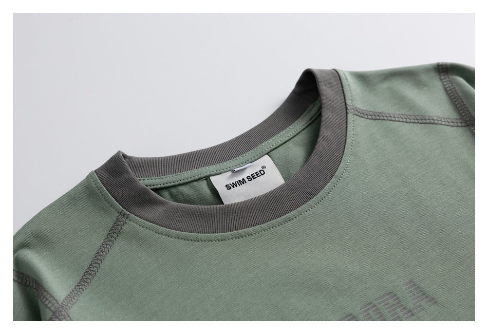 Close-up of the sage green T-shirt's charcoal ribbed crew neck, contrast stitching and neck label.