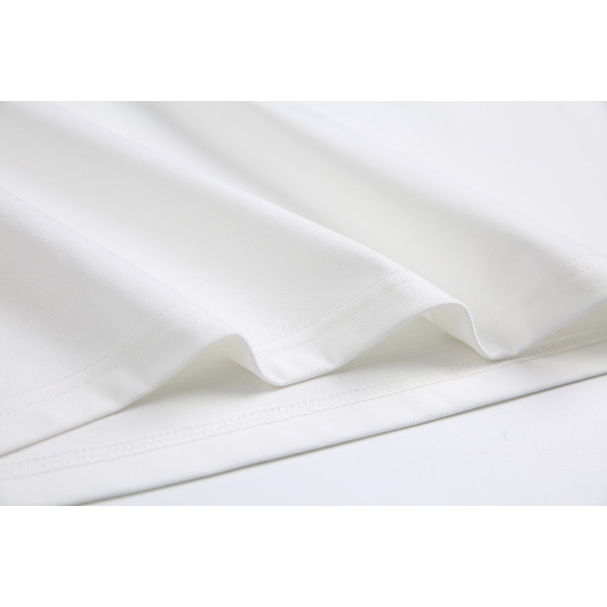 Close-up of the white T-shirt’s folded hem and visible stitching.
