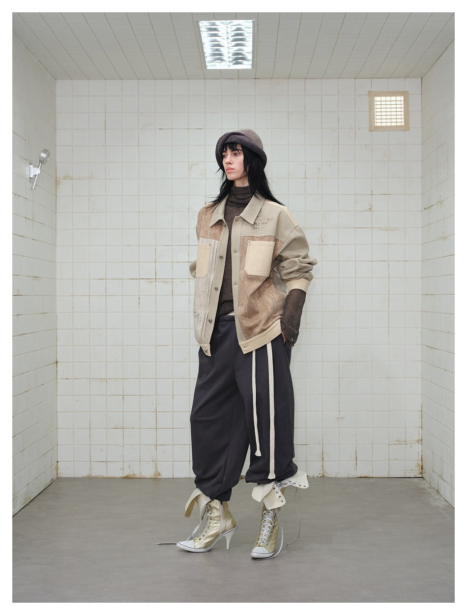 Model wearing the patchwork khaki and brown jacket open-posed in a tiled room with dark pants and gold high-top sneakers