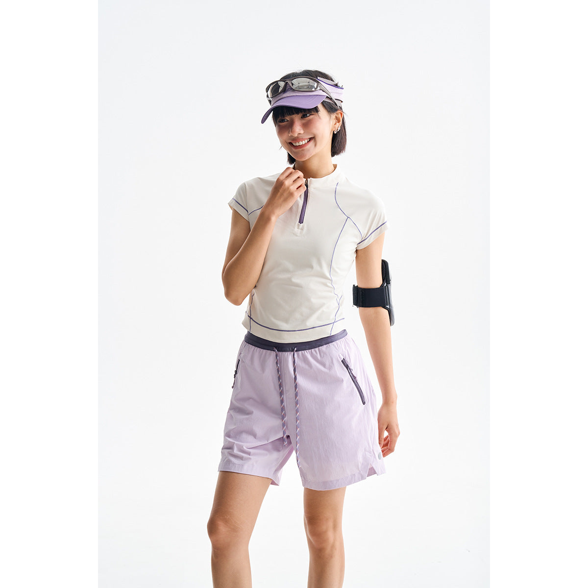 Model wearing a white short-sleeve quarter-zip top with purple piping and lavender shorts.