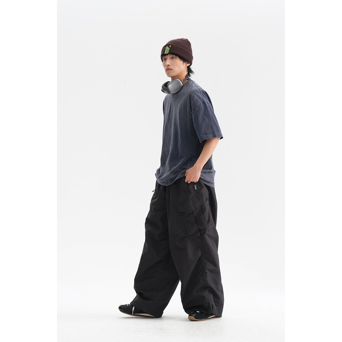 Model wearing loose black cargo trousers with a charcoal T-shirt, burgundy beanie and headphones.