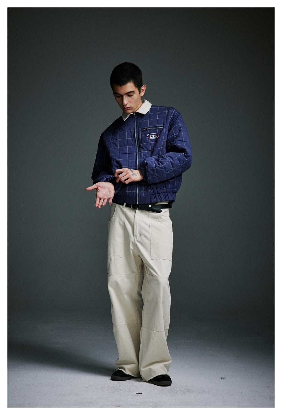 Model wearing a navy quilted jacket with cream collar and wide cream trousers, adjusting the jacket cuff.
