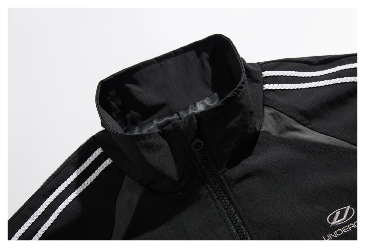 Close-up of a black track jacket's stand collar, front zipper, white shoulder stripes and embroidered chest emblem.