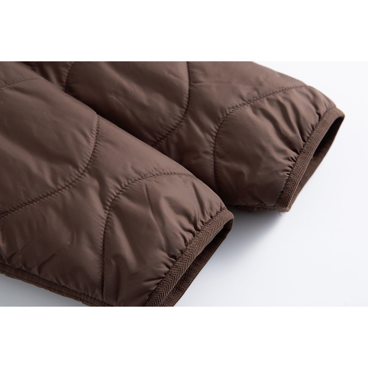 Close-up of the brown quilted jacket's sleeves and cuffs with patterned brown edge binding.