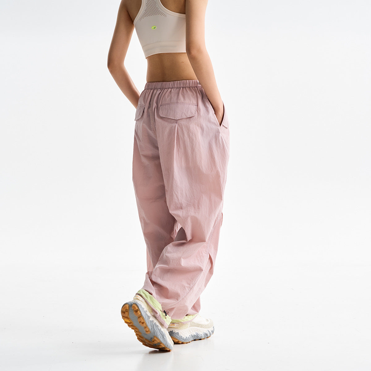 Rear view of a model wearing loose pale pink pants with an elastic waistband and two flap back pockets.