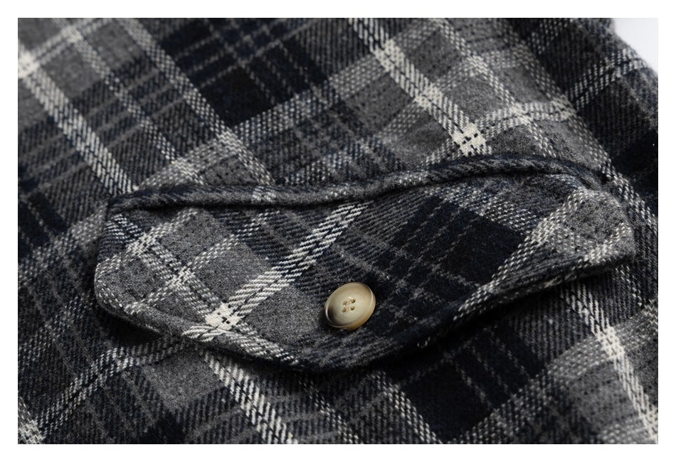 Close-up of a buttoned flap pocket on a charcoal and gray plaid jacket.