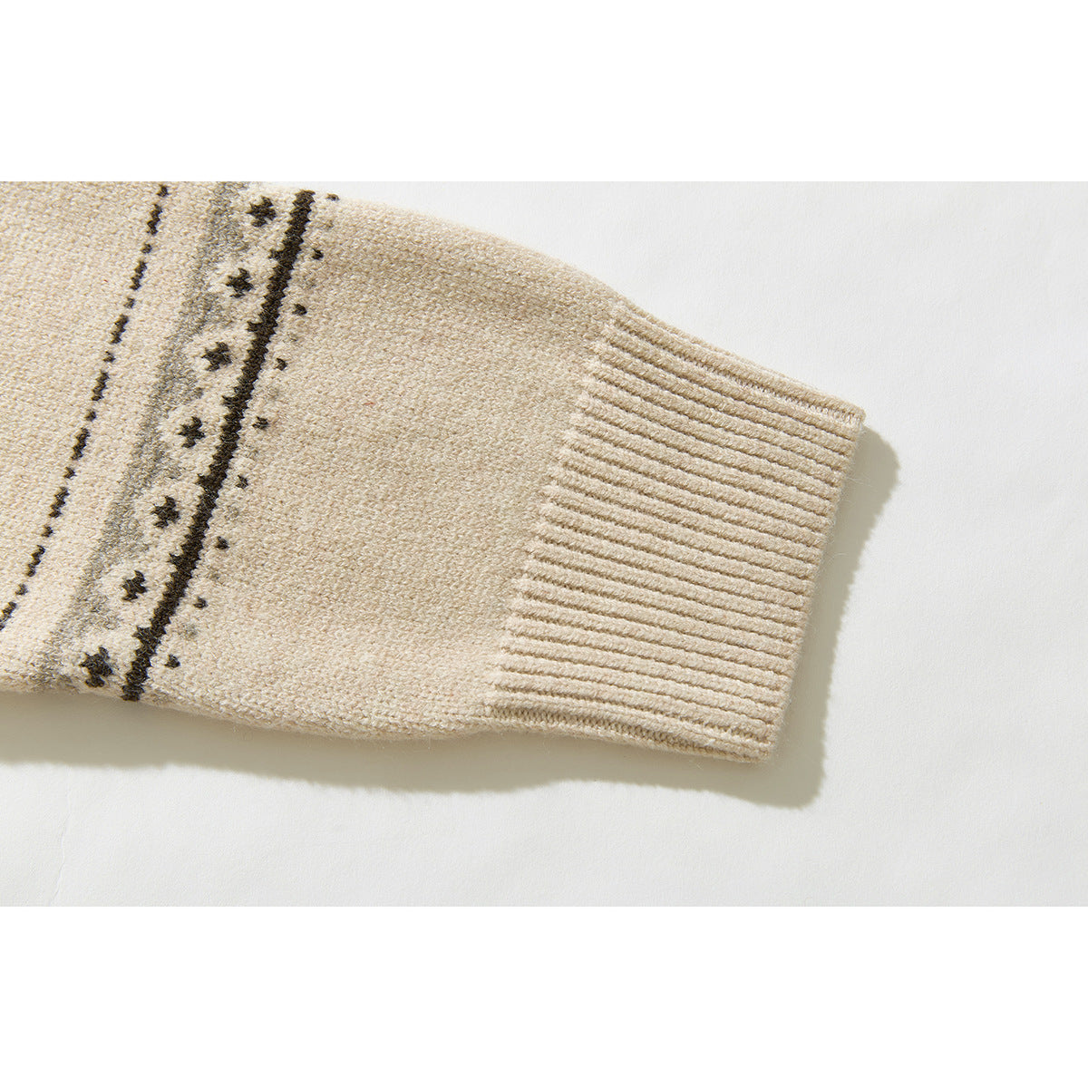 Close-up of a cream cardigan sleeve showing a ribbed cuff and dark patterned stripe.