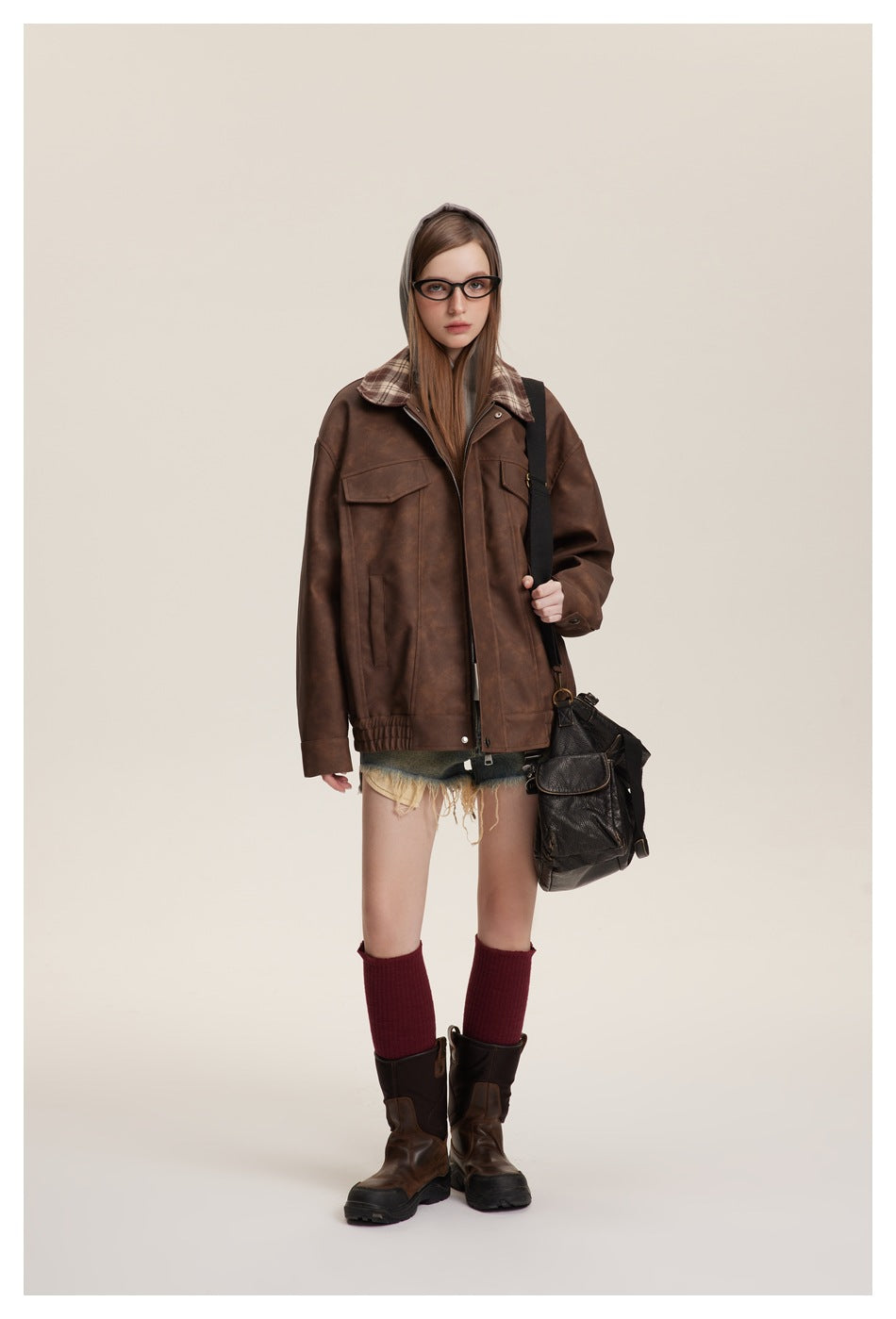 Model wearing the brown jacket zipped over a gray hoodie with shorts, red knee socks, boots and a black shoulder bag