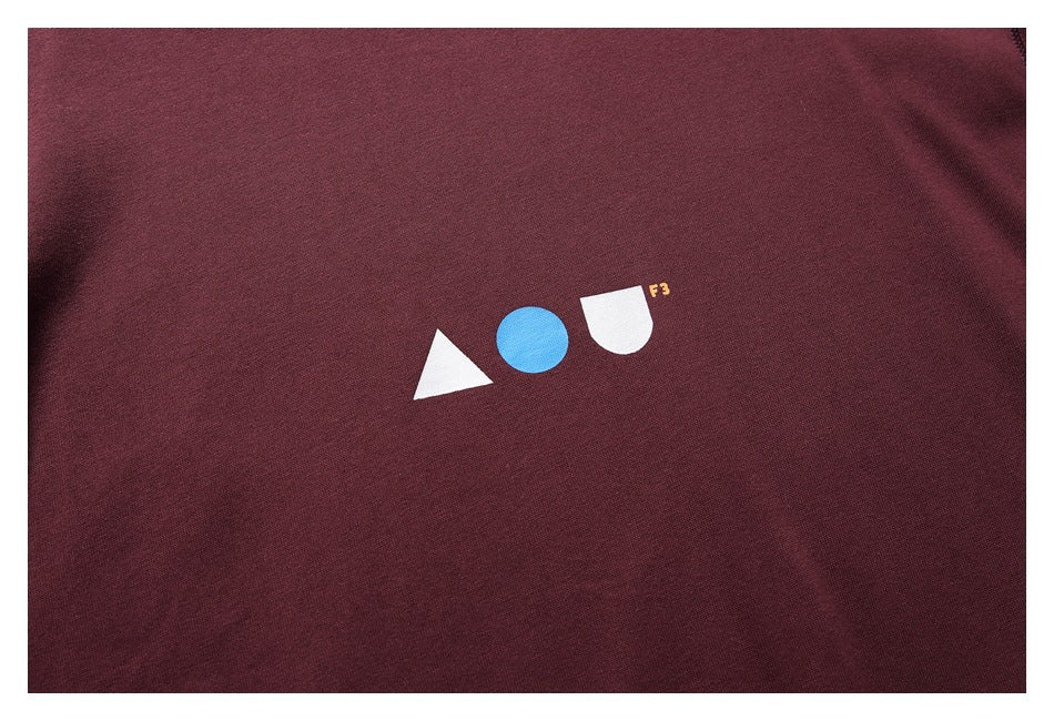 Close-up of a burgundy shirt with a small white-and-blue geometric chest graphic and tiny yellow F3 lettering.