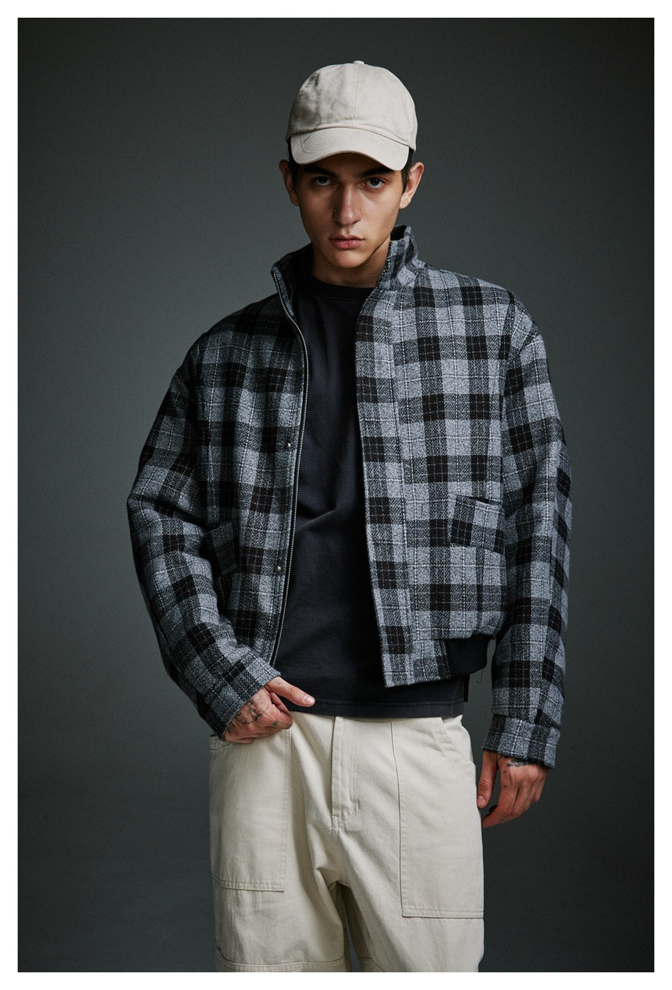 Model wearing an open gray-and-black plaid zip jacket over a black top with cream trousers.