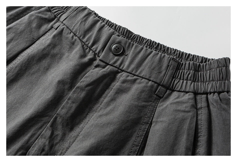 Close-up of charcoal pants showing the elasticated waistband, button closure, belt loop, and stitching.