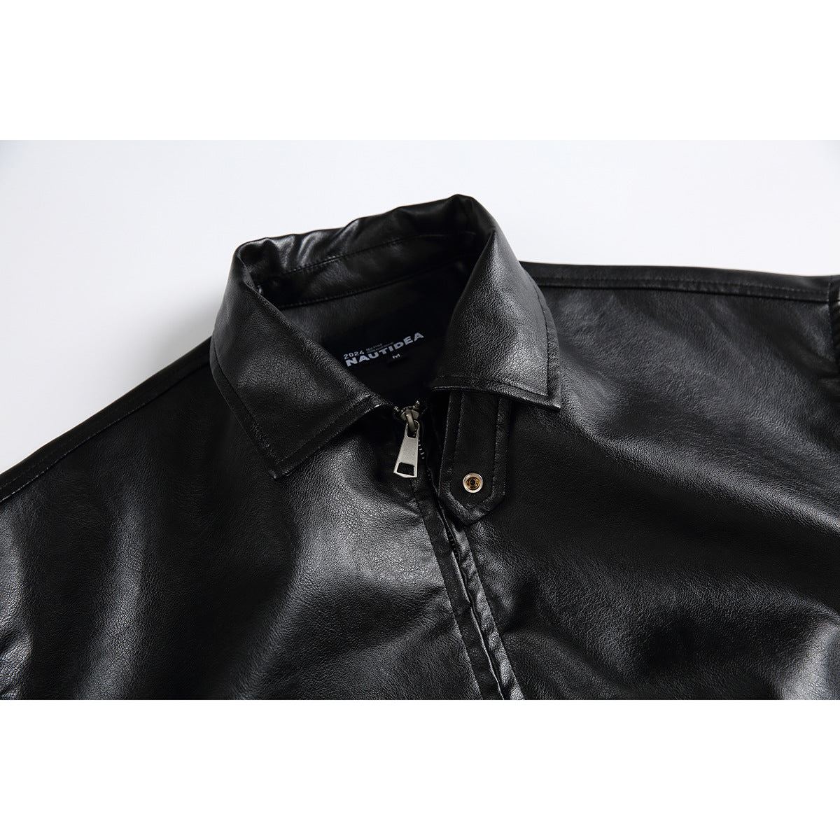 Close-up of a black jacket’s pointed collar, front zipper, and snap-tab detail.