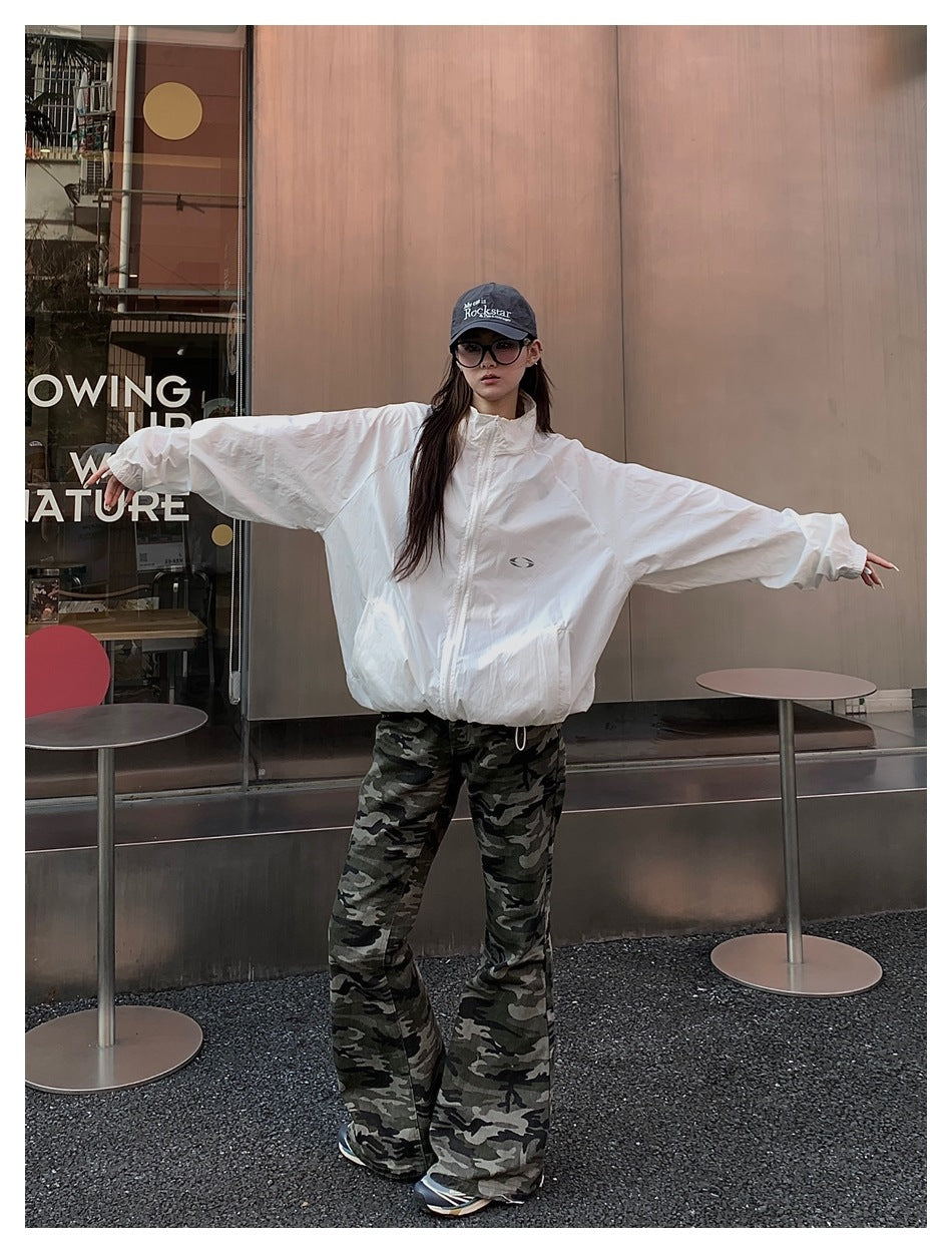 Front view of a model in a white oversized zip-up jacket with a small chest emblem and camouflage flared pants.