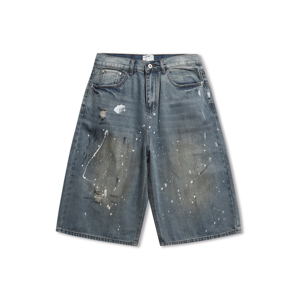 Front of faded blue distressed denim shorts with white paint splatters and smudged thigh patches on a white background