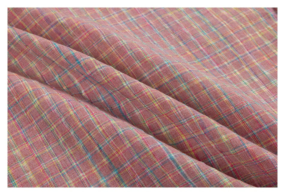 Close-up of pink plaid fabric with fine teal, yellow, and pale stripes.