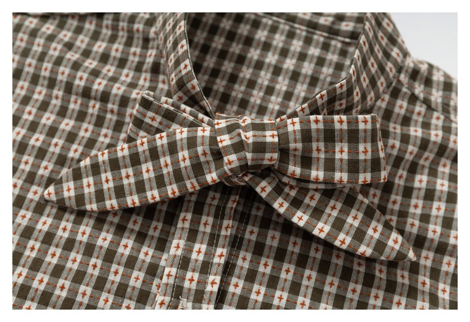 Close-up of a matching plaid bow tie against brown, white, and rust shirt fabric.