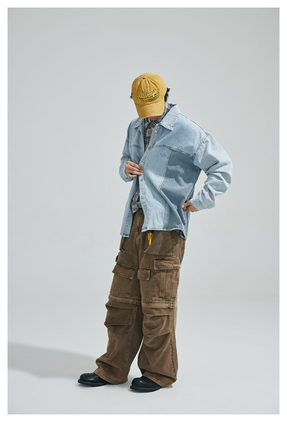 Model in a light blue patchwork denim jacket with a yellow cap, plaid shirt and brown cargo pants, head tilted down