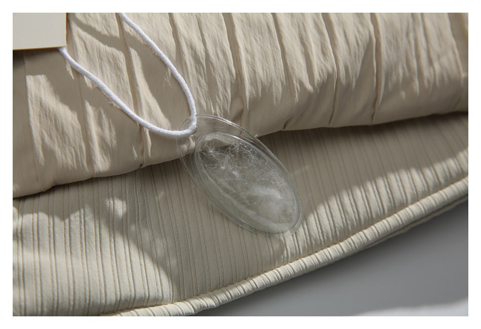 Close-up of cream crinkled quilted garment fabric with a clear oval fill sample hanging from a white cord.