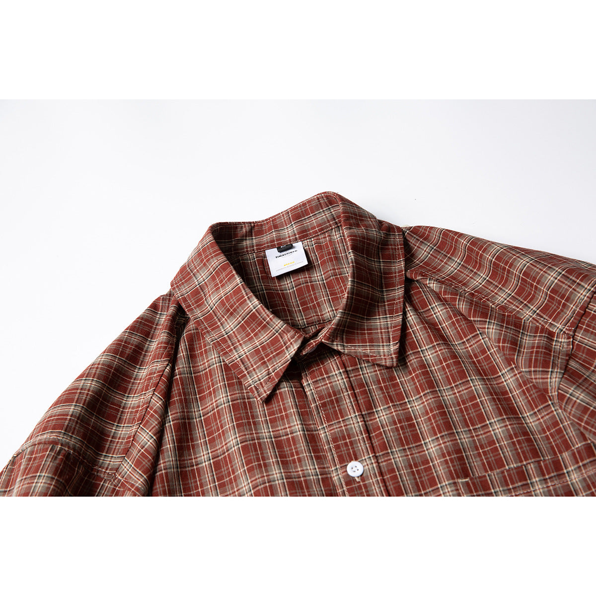 Close-up of a rust-red plaid short-sleeve shirt showing its pointed collar, front placket, and chest pocket.
