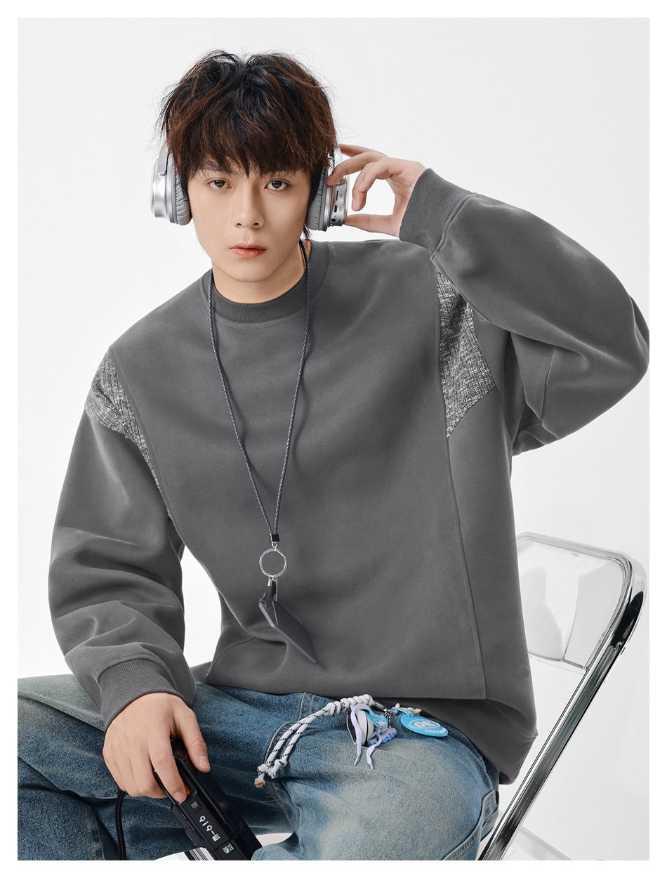 Model wearing dark gray crew-neck sweatshirt with textured shoulder panels, seated with headphones and jeans