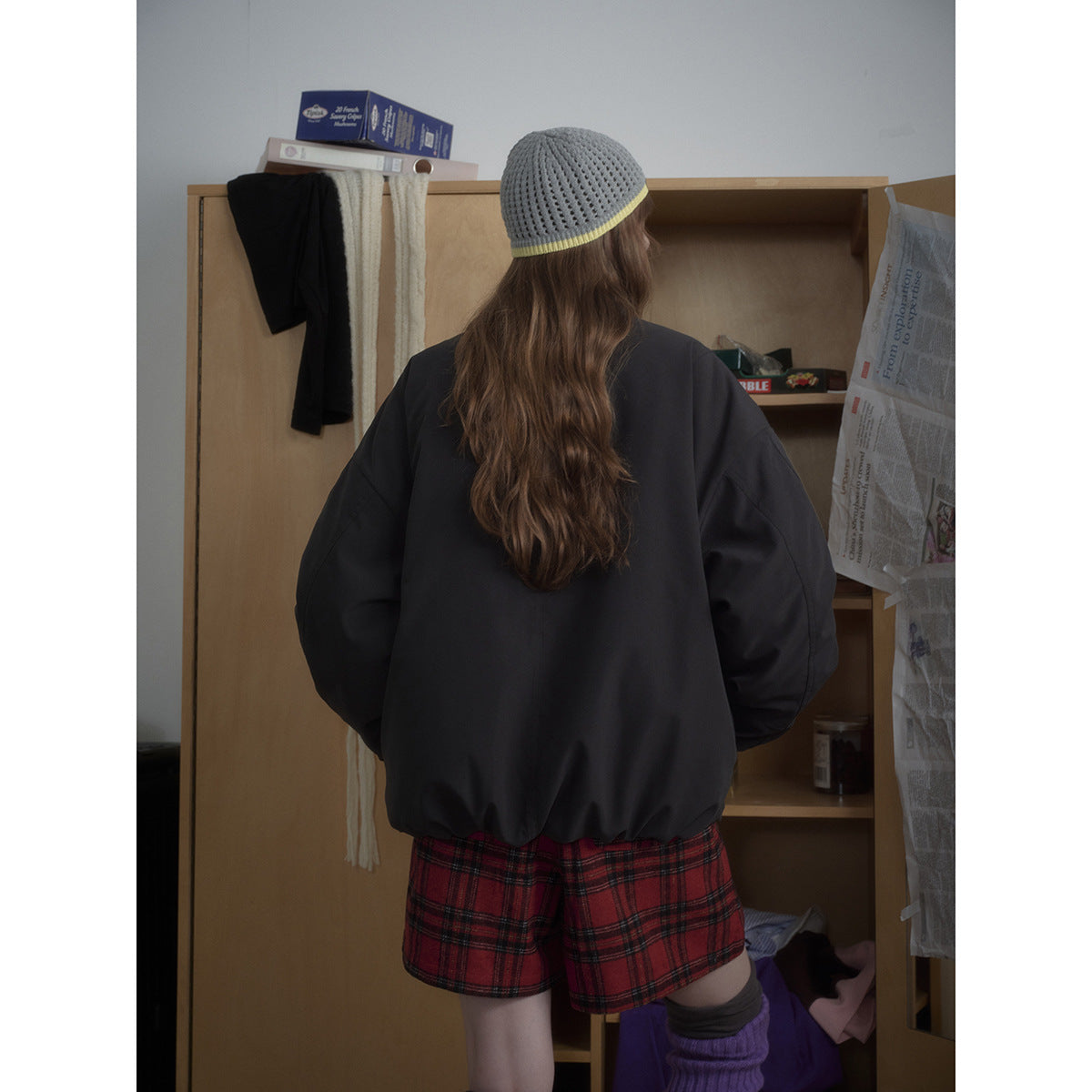 Back view of a model wearing an oversized black bomber jacket, red plaid shorts, and a gray knit beanie.