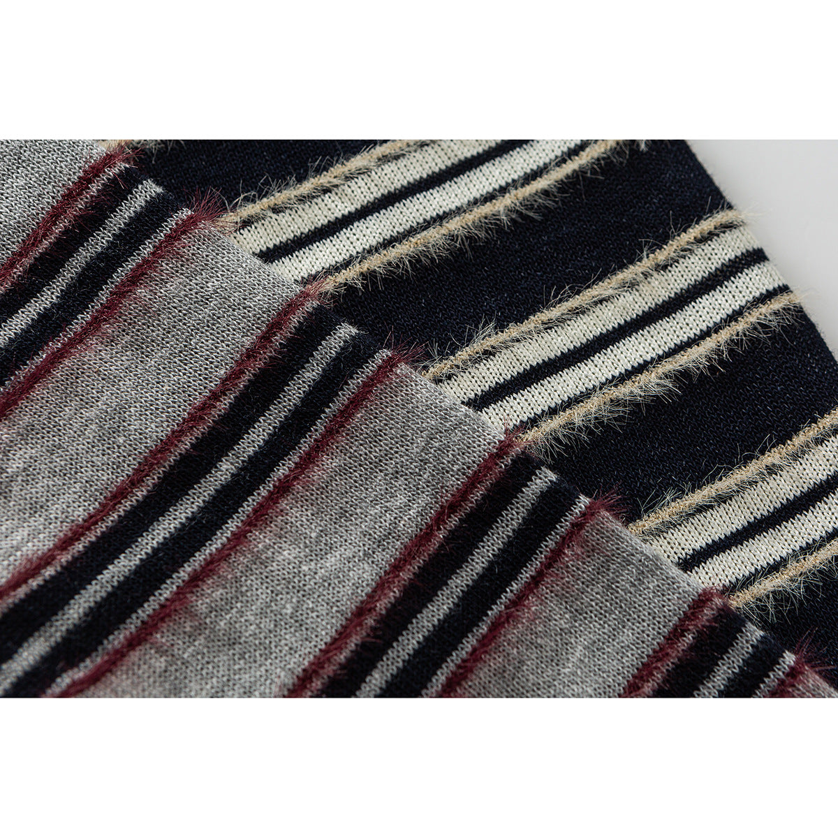 Close-up of knitted stripes in black, cream, gray, and burgundy with fuzzy beige yarn accents.