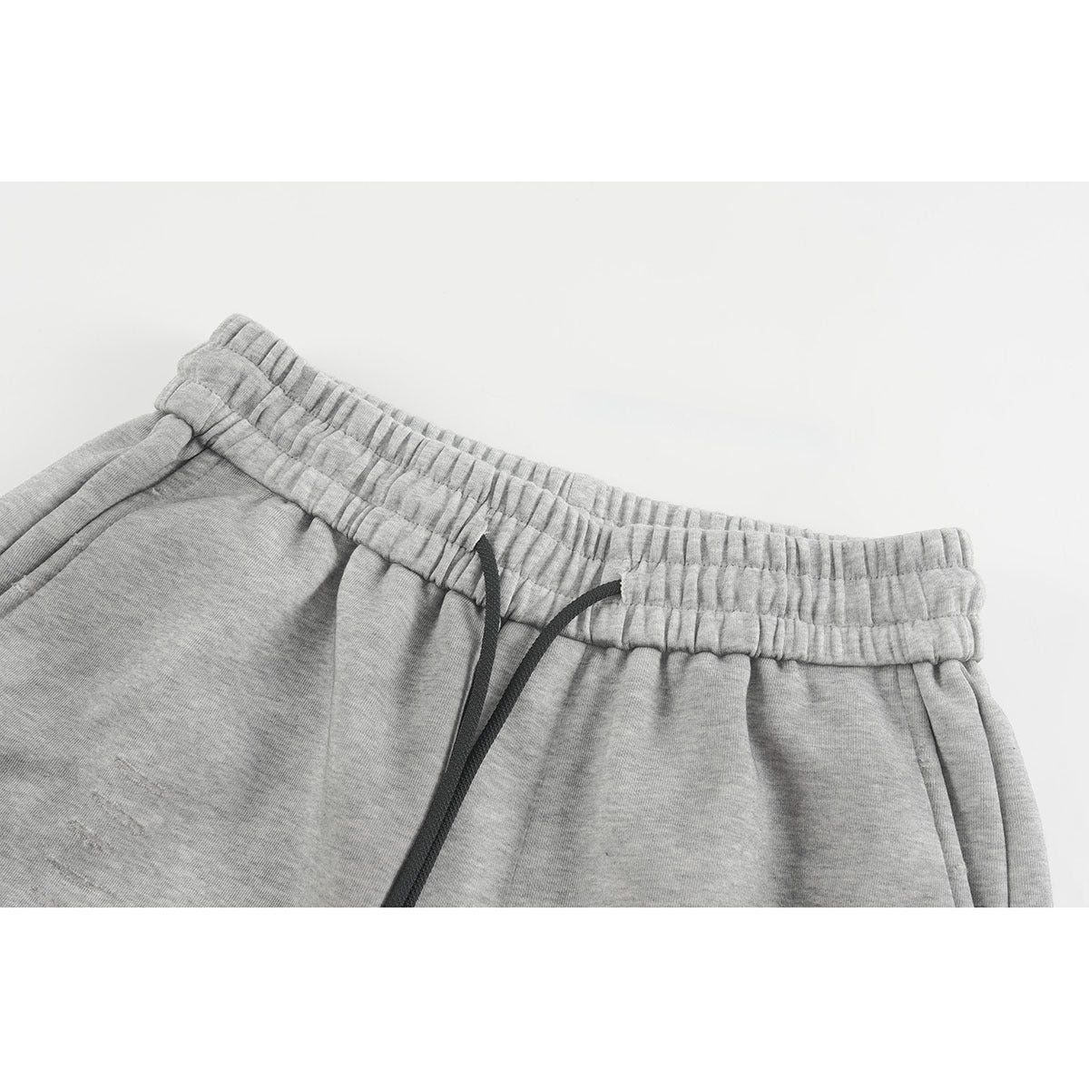 Close-up of light gray shorts showing the gathered elastic waistband, black drawstring, and side pockets.