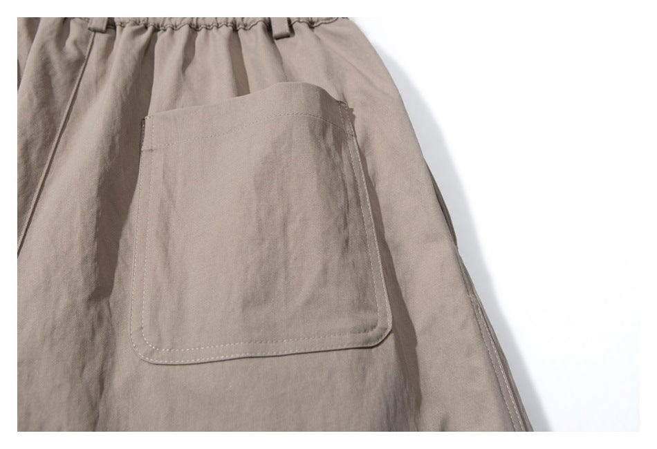 Close-up of a large stitched patch pocket on taupe trousers.