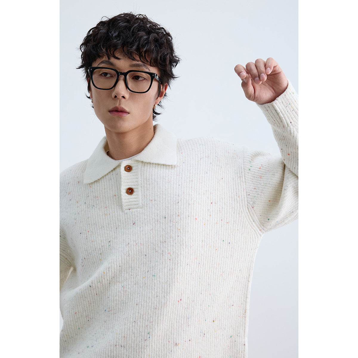 Close view of a model wearing an ivory speckled knit polo sweater with a wide collar and brown buttons.