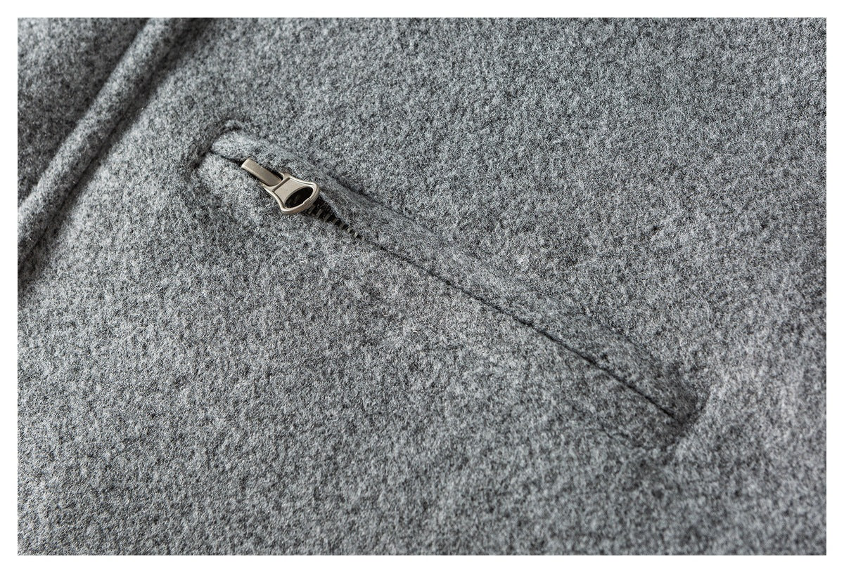 Close-up of a slanted zip pocket on gray textured coat fabric.