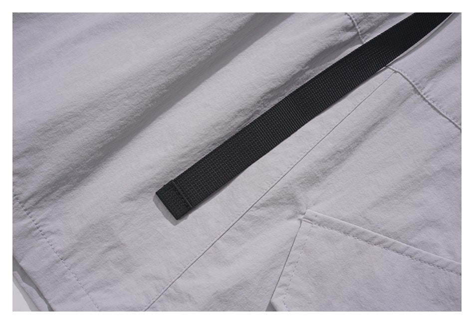 Close-up of a black webbing strap lying across the stitched panels of light gray bottoms.