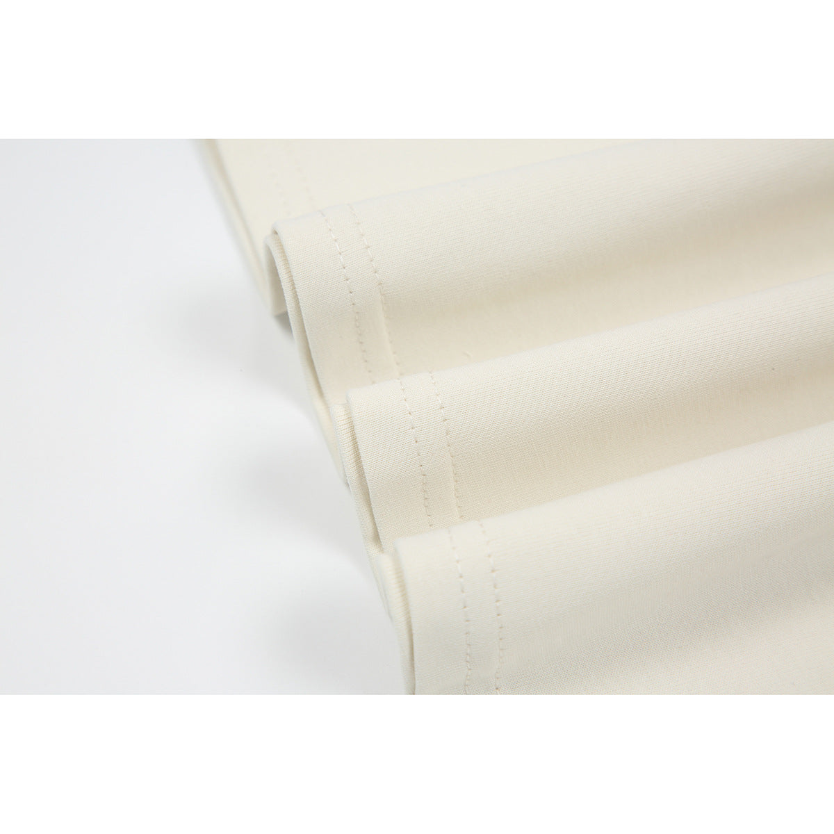 Close-up of the ivory shirt's folded hem and parallel rows of stitching.