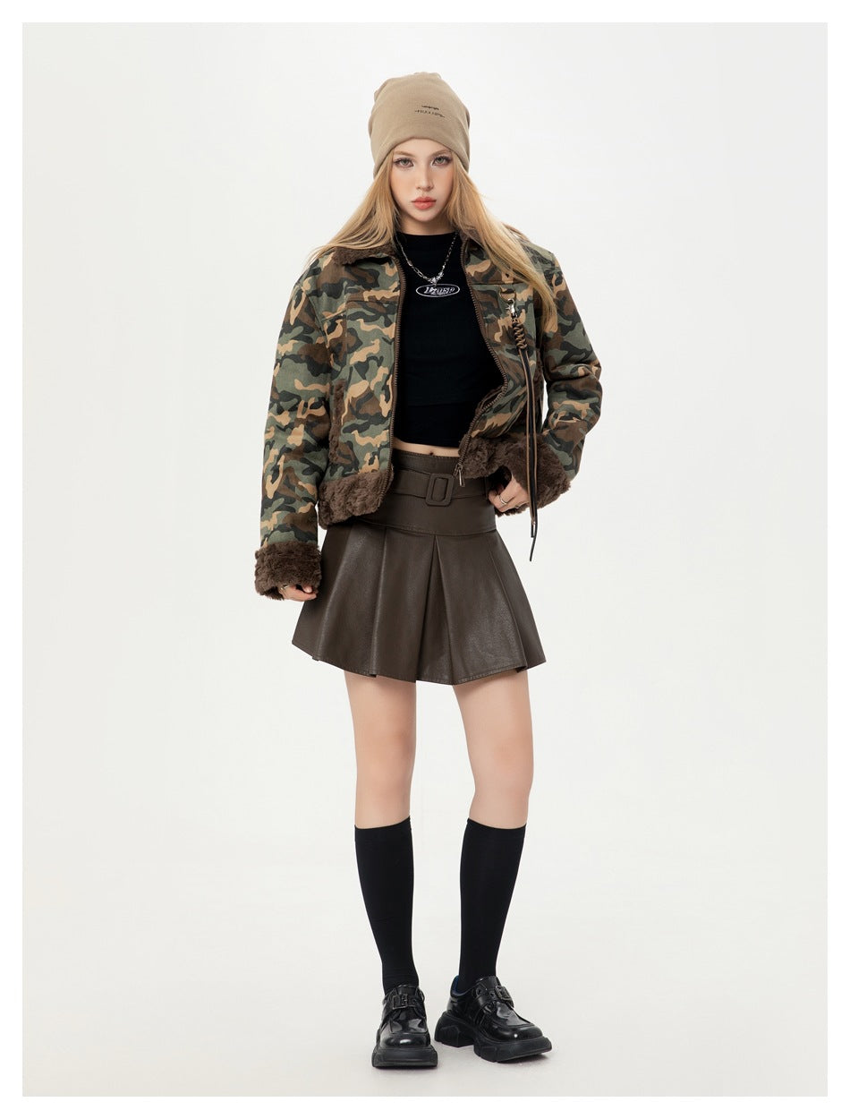 Model standing in a camouflage jacket with fleece-like trim, black top, brown pleated skirt and knee socks