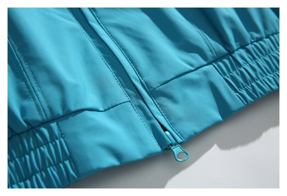 Close-up of the turquoise jacket's gathered hem and front zipper with a loop pull.
