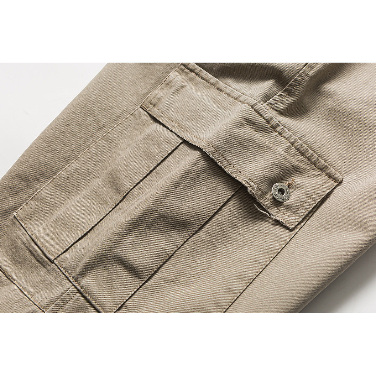 Close-up of a beige cargo trouser leg showing a large flap pocket with a button.