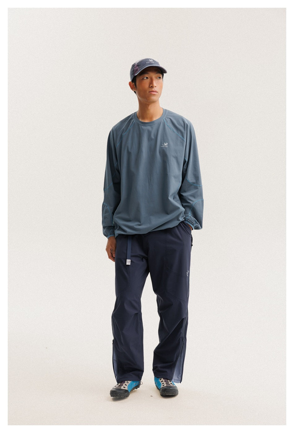 Front view of a model wearing a blue-gray long-sleeve pullover with cyan seams and navy pants.