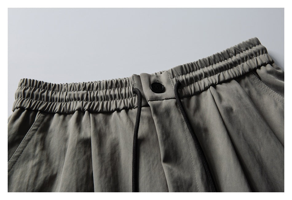 Close-up of gray trousers showing an elastic waistband, black button, drawstrings, and front pleats.