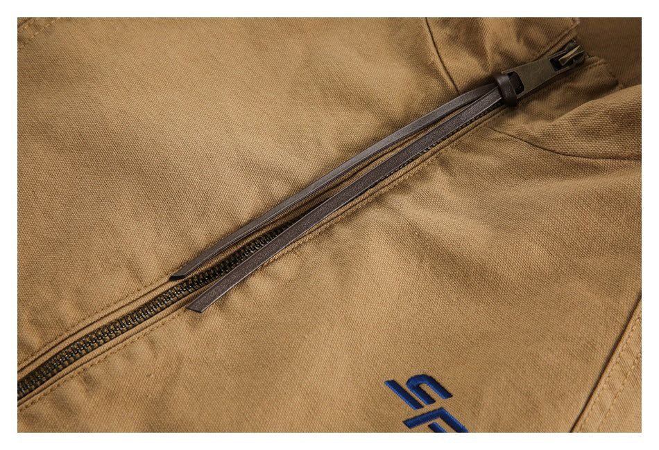 Close-up of a tan jacket's dark diagonal zipper and blue embroidered emblem.