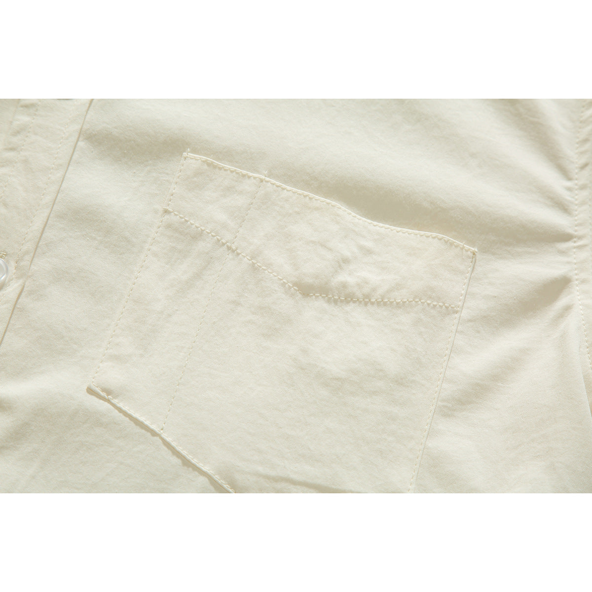 Close-up of the ivory shirt's stitched chest pocket and curved pocket opening.