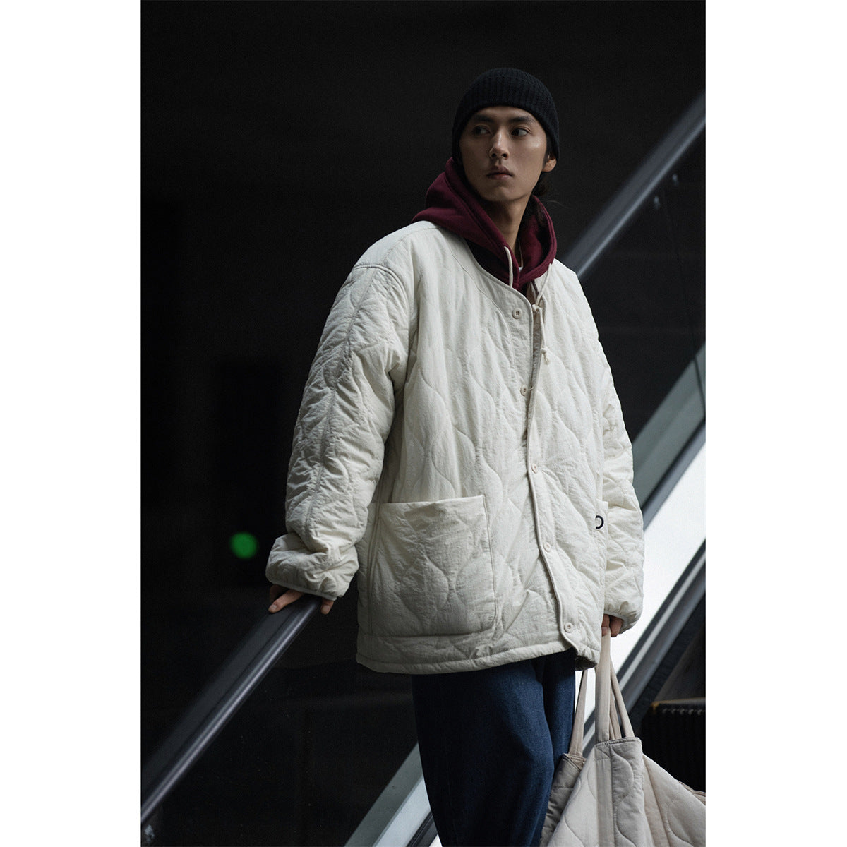 Model wearing an oversized ivory quilted jacket with a button front and large patch pockets.
