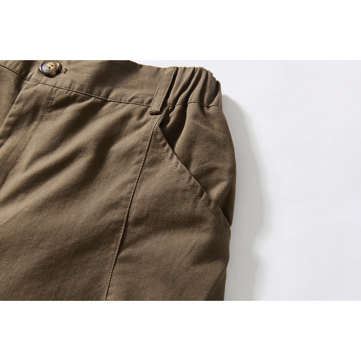 Close-up of brown shorts showing an angled front pocket, elastic at the waistband, and a button.