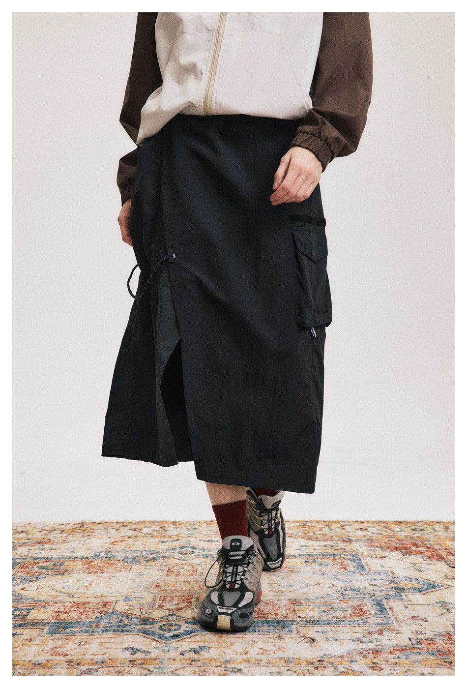 A person wears a black below-knee wrap skirt with a flap cargo pocket and side drawcord.