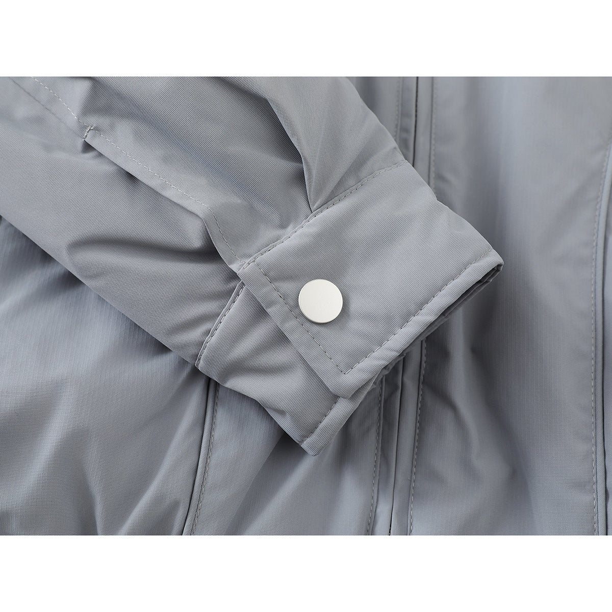 Close-up of a light gray jacket sleeve cuff with a round snap button.