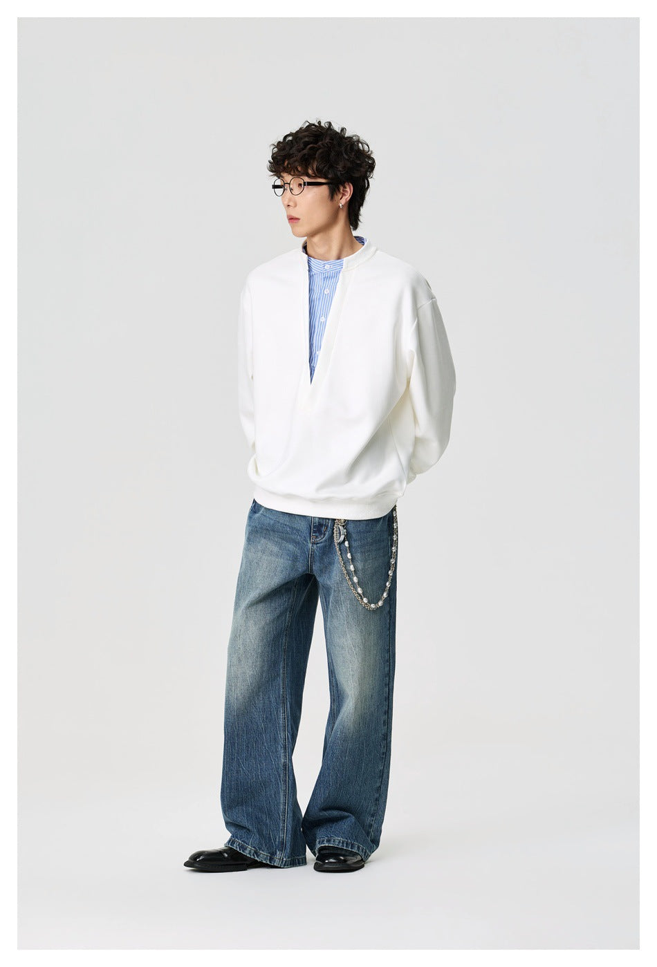 Full-length model wearing a white oversized split-neck pullover with loose blue jeans.